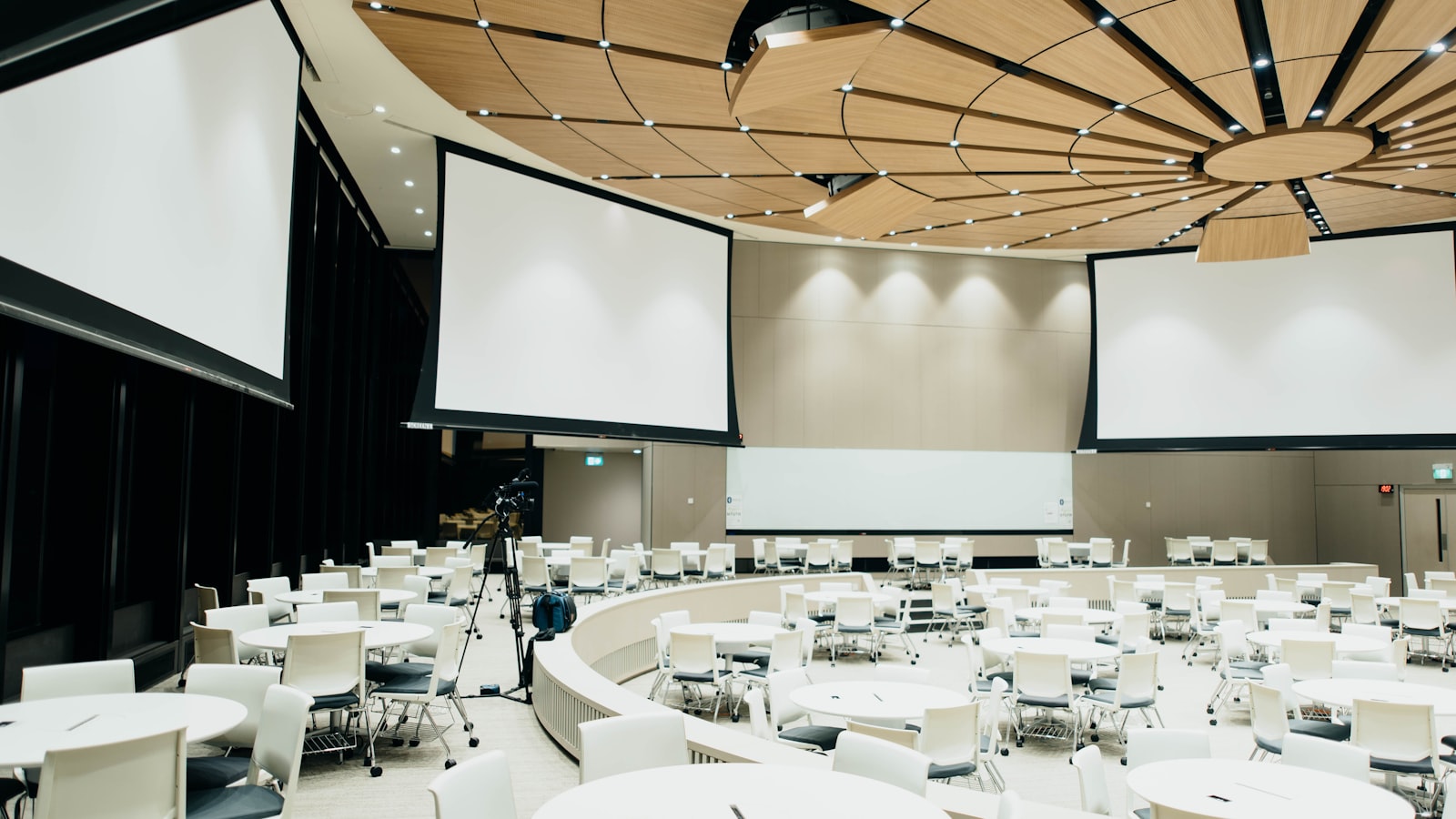 Empty hotel function room with round tables set beneath three projection screens